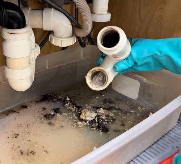 Plumber disassembling clogged kitchen sink P-trap filled with heavy cooking grease and food sludge in Houston, TX 77002